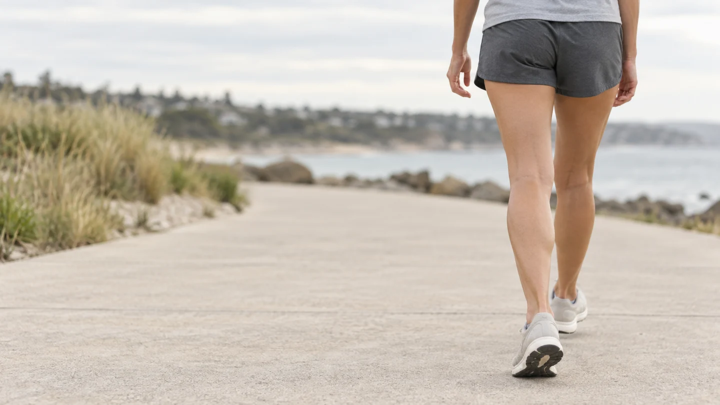 Illustrative scene of a person walking along a coastal path, showing their legs and stride.