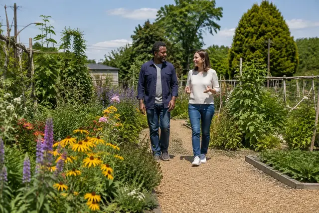 Illustrative photograph of two adults talking while walking along a path through a flowering community garden.
