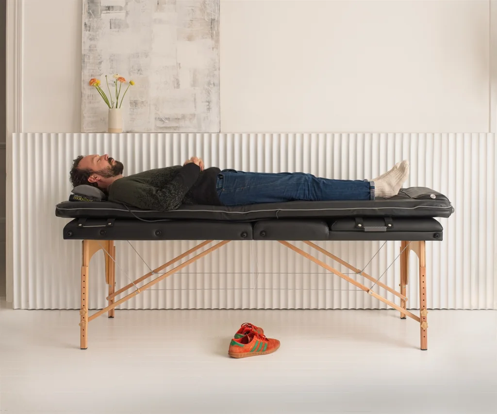 Manufacturer demonstration of a person lying on the Mobiliser, supported on a treatment table.