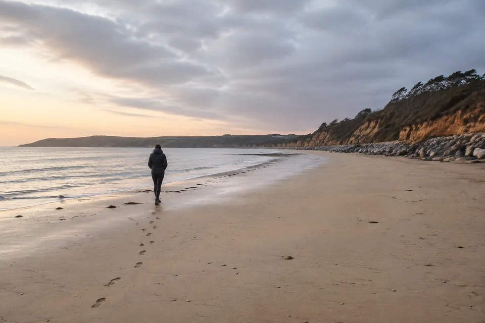 Illustrative photograph of a person walking along a sheltered beach, with footprints in the sand and soft coastal light.