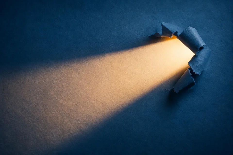 Editorial illustration of warm light shining through an opening in textured blue paper.
