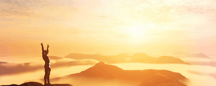 Silhouette of a person with arms raised on a mountaintop at sunrise.